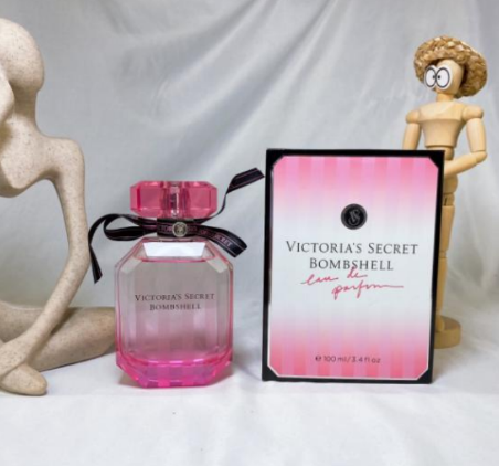 Pink Victoria's Secret Bombshell perfume bottle and packaging on a white surface with decorative figures.